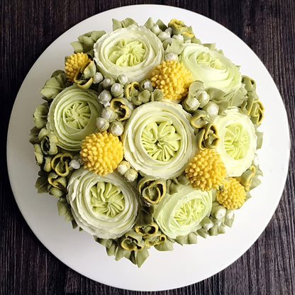 Gâteau rond entièrement décoré de fleurs sculptées en crème au beurre dans les tons vert et jaune